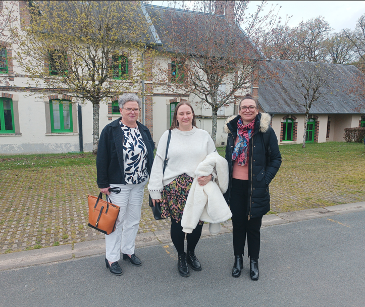 Trois femmes se tiennent ensemble à l’extérieur, devant une maison, en posant pour une photo.